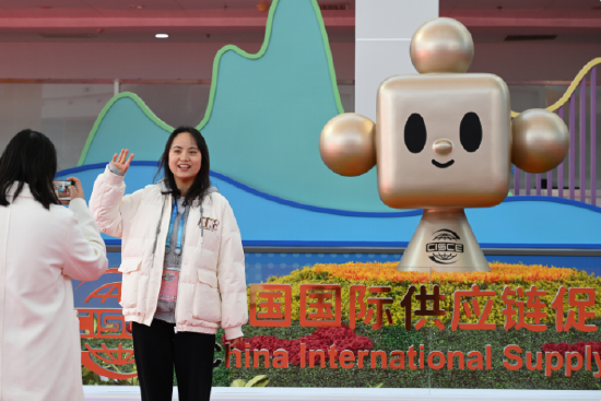 11月29日，参观者在摆放着链博会吉祥物“链氪”标识的花坛前留影。新华社记者 李贺 摄